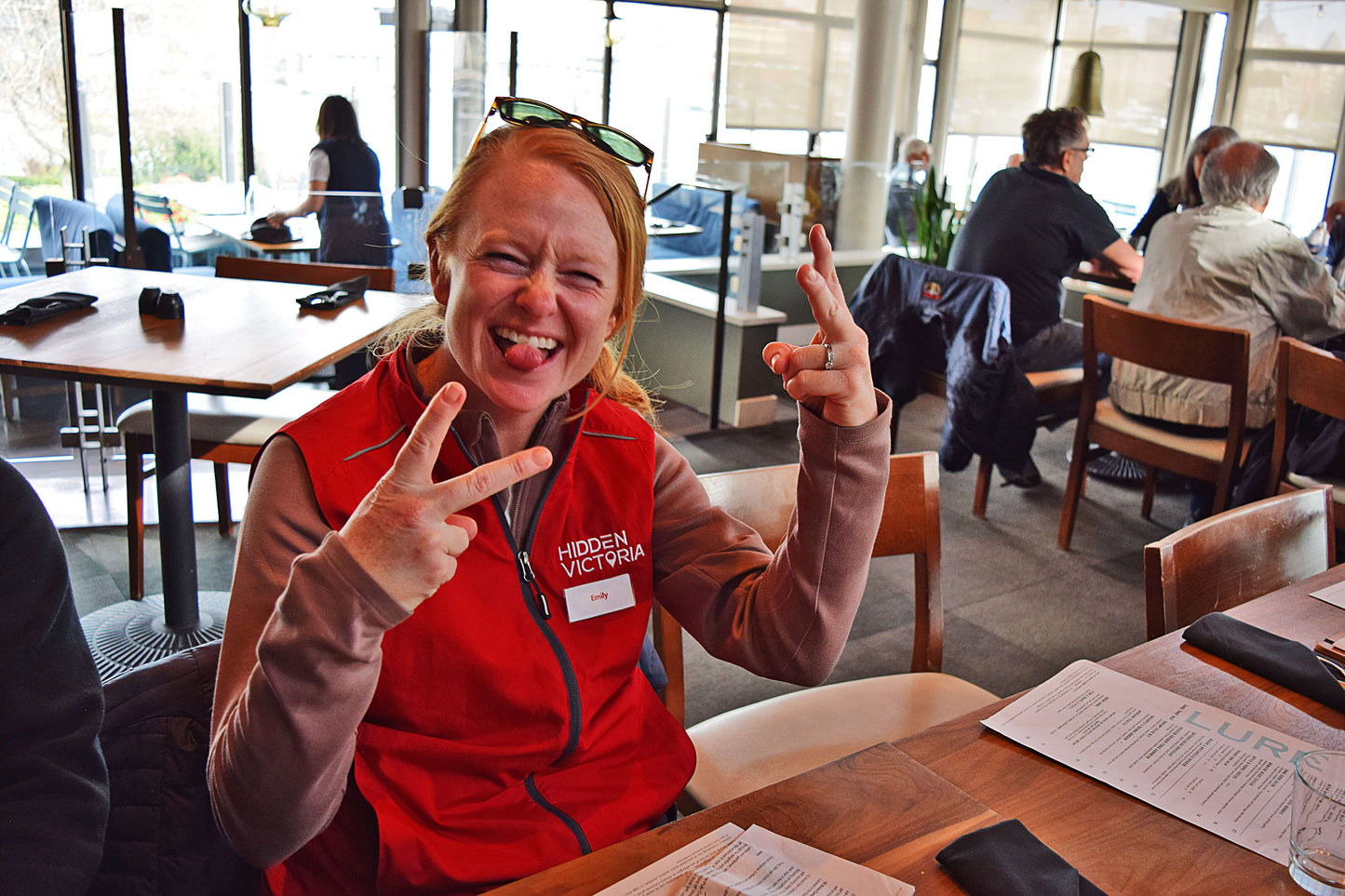 Person in a Hidden Victoria vest making a peace sign in a casual dining setting
