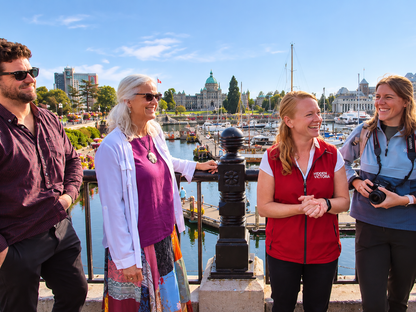 Four people standing outdoors with the Victoria Parliament  in the background. Hidden Victoria guide tells stories as her guests listen