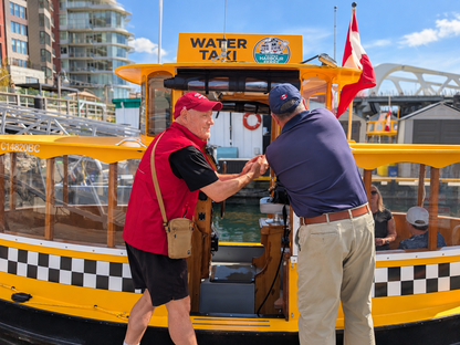 A bright yellow water taxi boat docked at a harbor with two men shaking hands at the open front door. The guide and the captain have worked along side each other for a long time